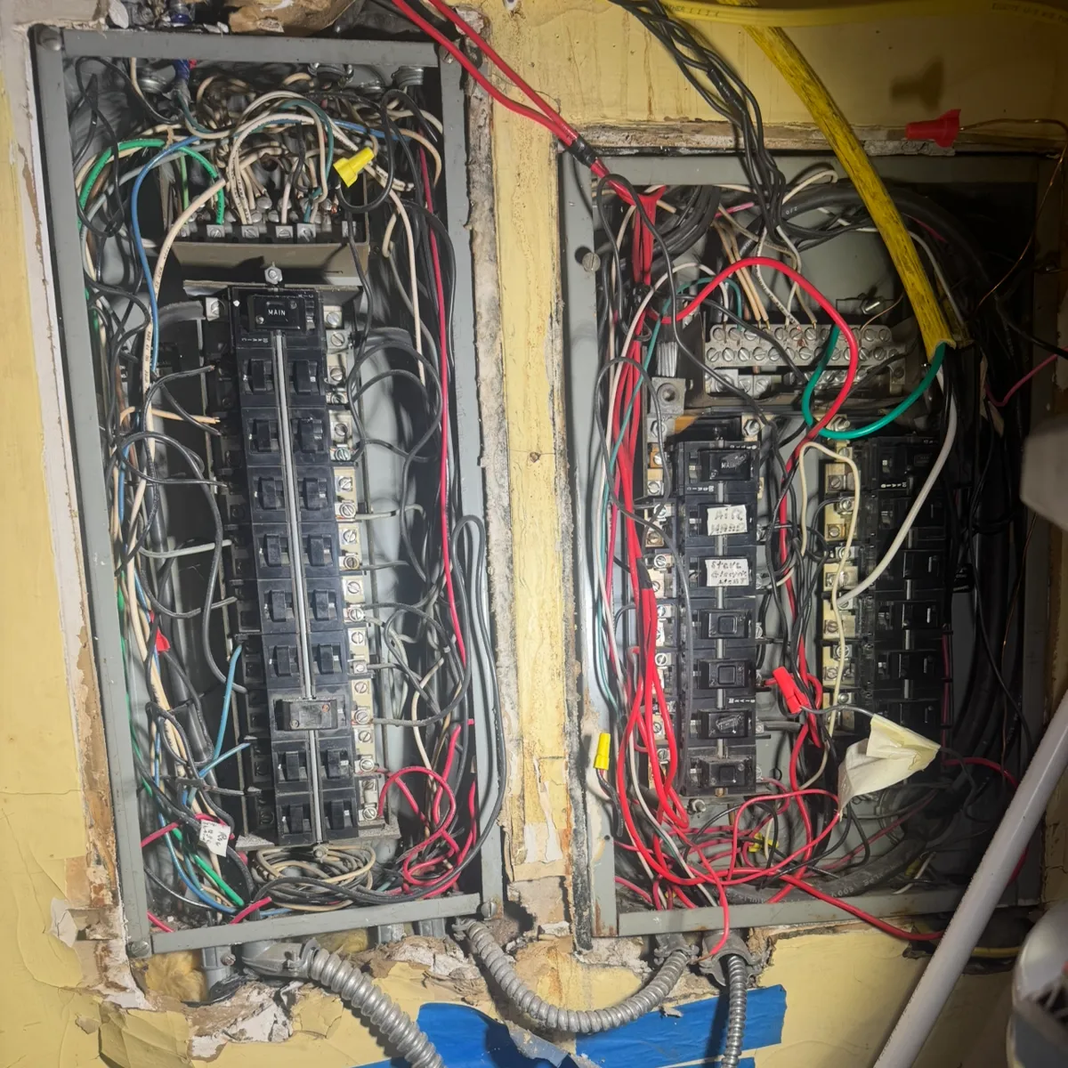 Two aged service panels side by side with covers off, original wiring exposed