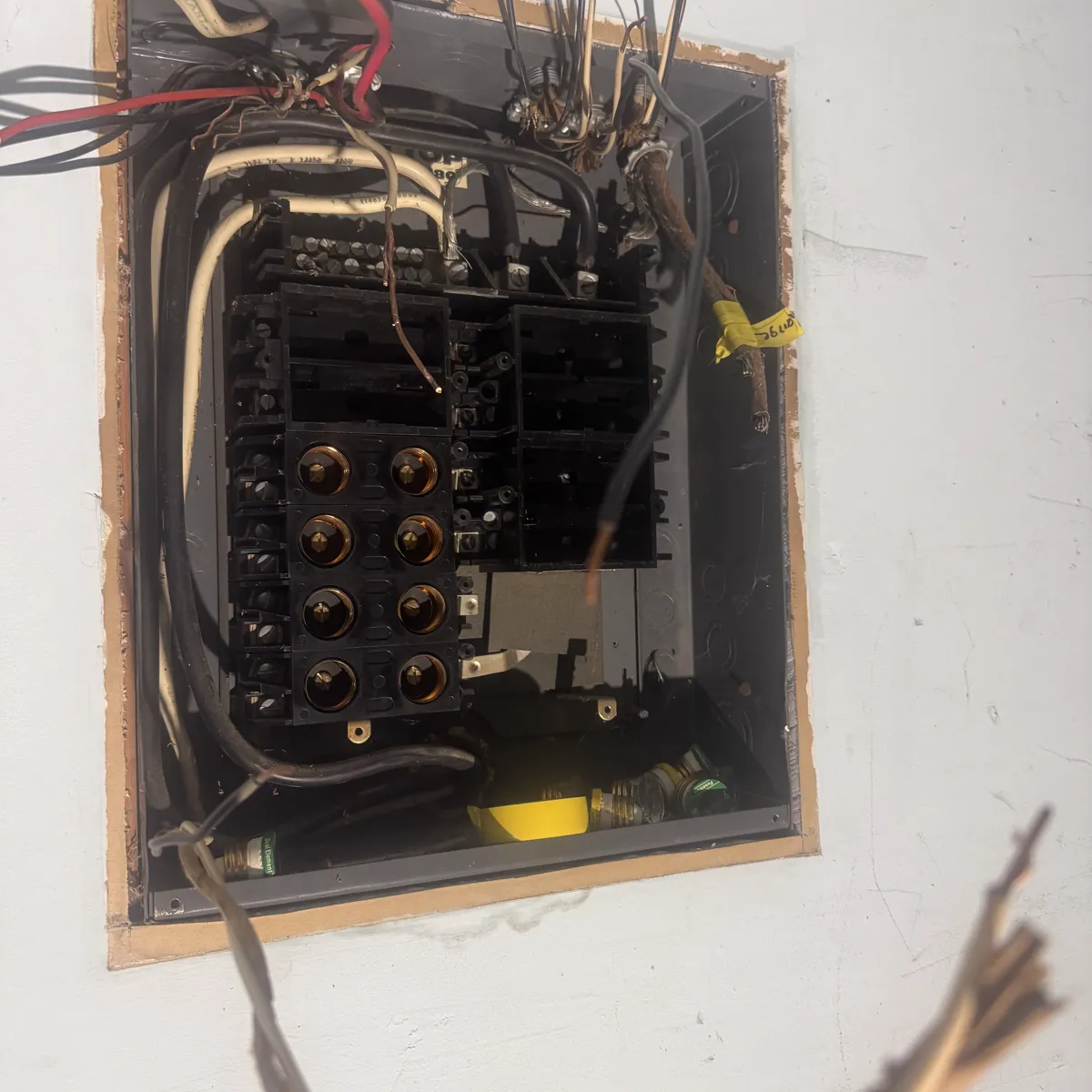 An original panel opened in a plaster wall, aged conductors hanging below